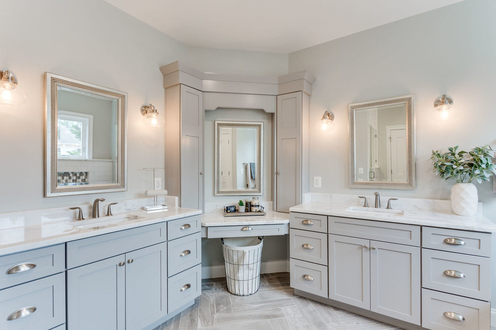 Diseño de cuarto de baño principal tradicional con armarios estilo shaker, puertas de armario grises, paredes grises, lavabo bajoencimera, suelo gris, encimeras blancas y espejo con luz