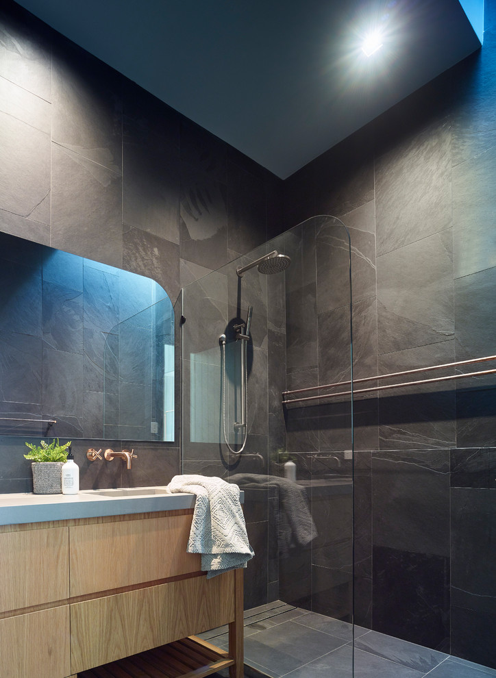 Bild på ett funkis grå grått badrum, med släta luckor, skåp i ljust trä, en kantlös dusch, svart kakel, grå kakel, svarta väggar, ett integrerad handfat, grått golv och med dusch som är öppen