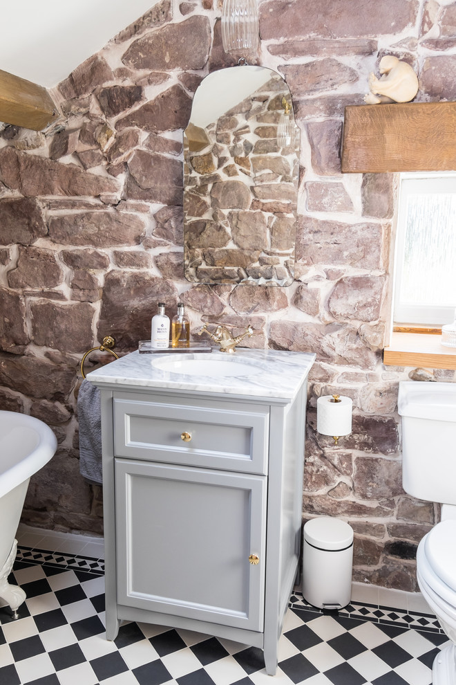 Klassisk inredning av ett litet badrum för barn, med möbel-liknande, grå skåp, ett badkar med tassar, en dusch/badkar-kombination, en toalettstol med separat cisternkåpa, svart och vit kakel, porslinskakel, grå väggar, klinkergolv i porslin, ett undermonterad handfat och marmorbänkskiva