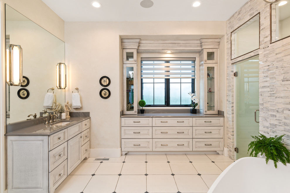 Inredning av ett lantligt stort grå grått en-suite badrum, med luckor med infälld panel, ett fristående badkar, marmorkakel, klinkergolv i keramik, ett undermonterad handfat, bänkskiva i kvarts, beige skåp, en dusch i en alkov, beige kakel, grå kakel, beige väggar, beiget golv och dusch med gångjärnsdörr