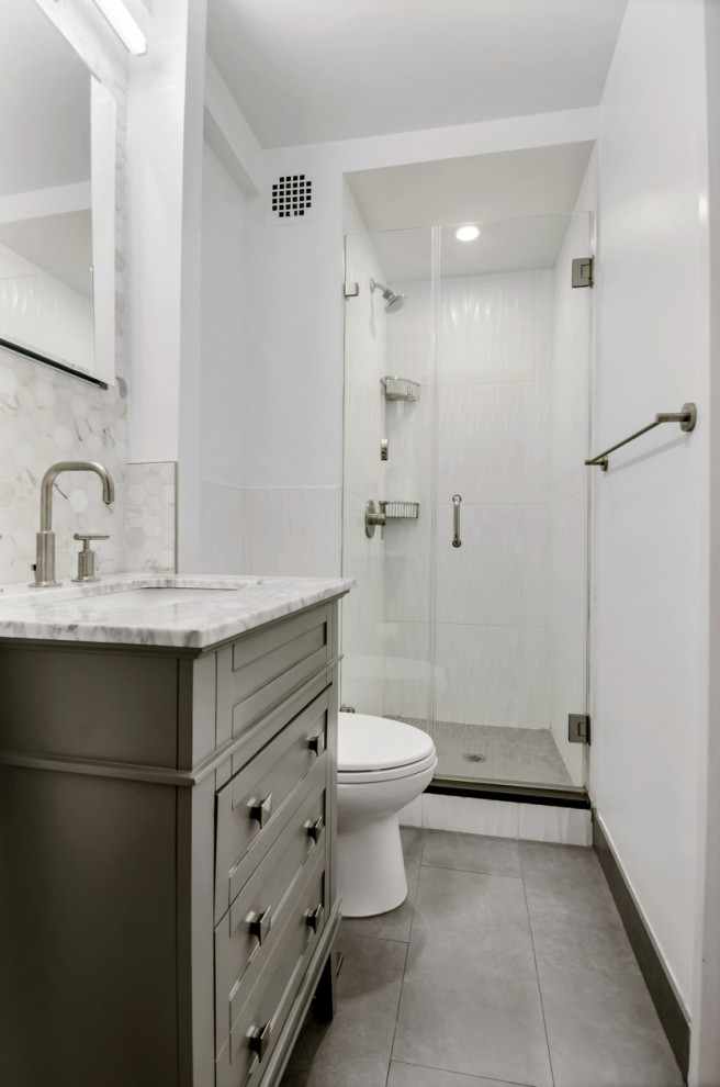 Example of a mid-sized classic kids' white tile and porcelain tile porcelain tile and gray floor bathroom design in New York with shaker cabinets, a one-piece toilet, an undermount sink, marble countertops, multicolored countertops, gray cabinets, gray walls and a hinged shower door