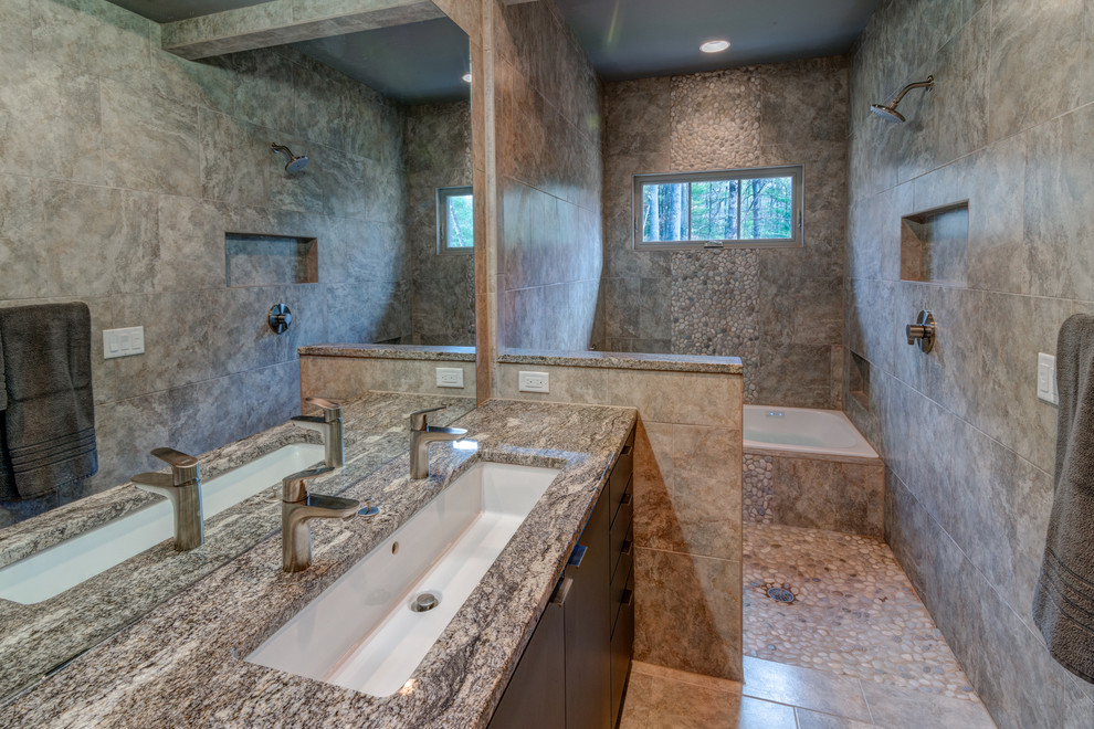 Cette image montre une salle de bain principale design en bois foncé avec une grande vasque, un placard à porte plane, un plan de toilette en granite, une baignoire posée, un combiné douche/baignoire, une plaque de galets et un sol en carrelage de porcelaine.