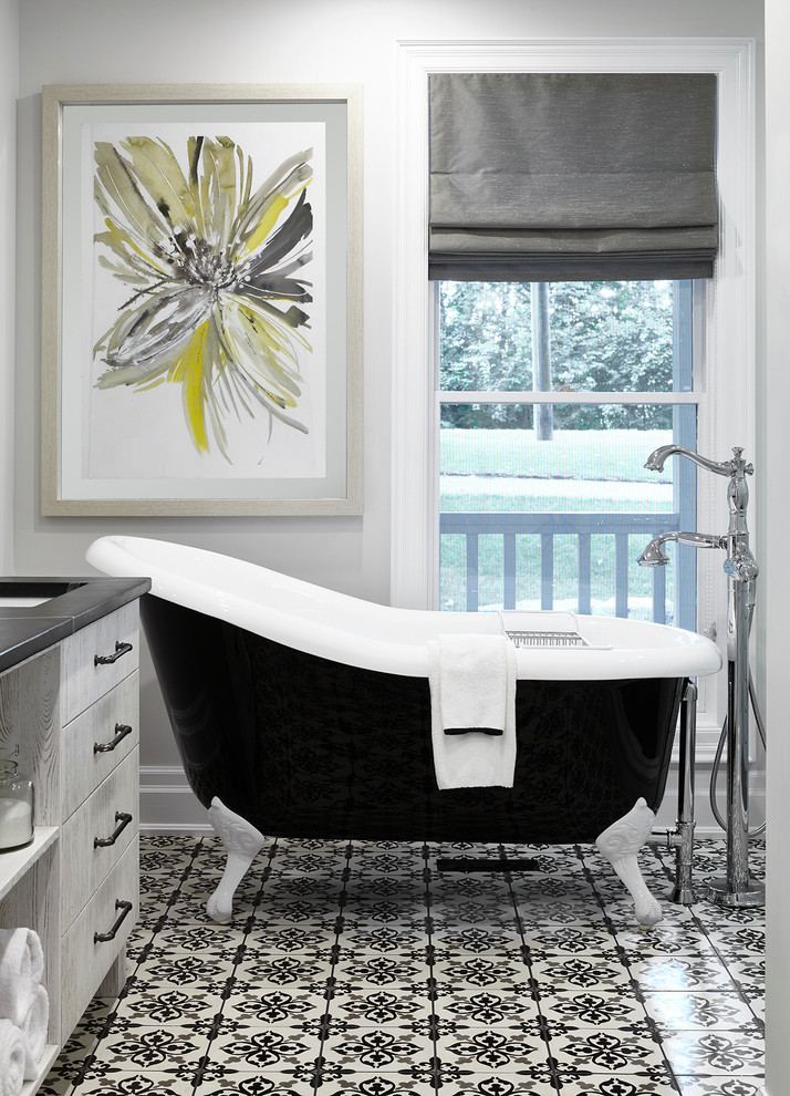 Cette photo montre une salle de bain principale chic avec un placard à porte plane, des portes de placard grises, une baignoire sur pieds, un carrelage noir et blanc, un mur gris et du carrelage bicolore.