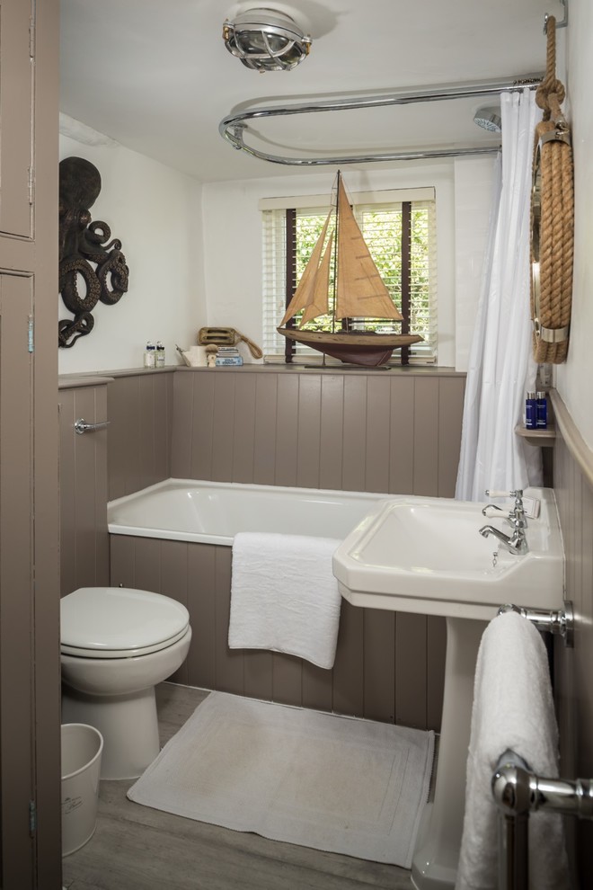 Bild på ett litet maritimt badrum för barn, med ett platsbyggt badkar, en dusch/badkar-kombination, en toalettstol med hel cisternkåpa, brun kakel, vita väggar, ljust trägolv, ett piedestal handfat, grått golv och dusch med duschdraperi