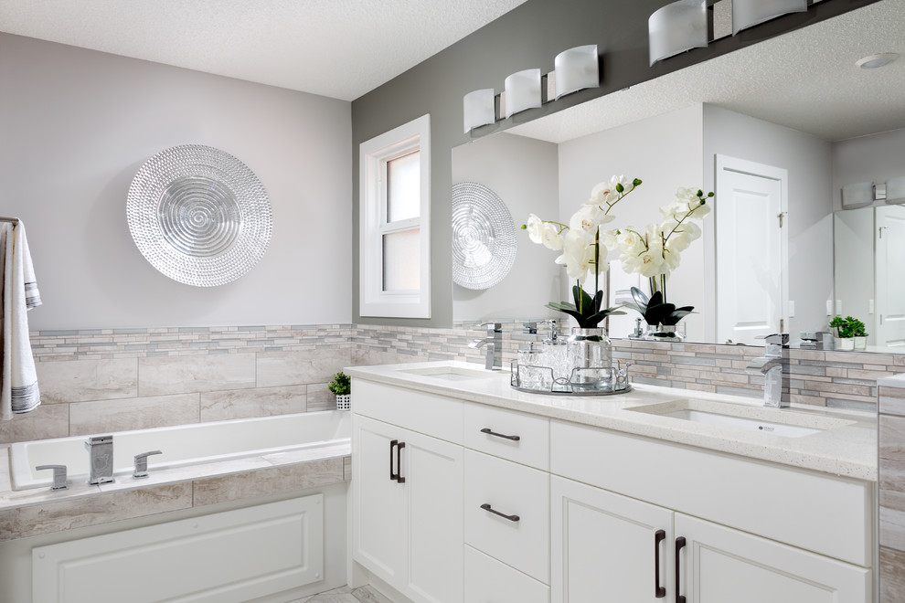 Immagine di una stanza da bagno tradizionale con ante con riquadro incassato, ante bianche, vasca da incasso, piastrelle beige, pareti grigie, lavabo sottopiano, pavimento grigio e top bianco