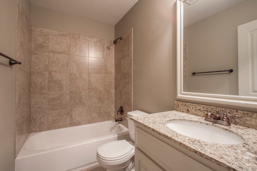 Photo of a medium sized traditional bathroom in Kansas City with raised-panel cabinets, white cabinets, granite worktops, a built-in bath, beige tiles, ceramic tiles, grey walls, ceramic flooring, a shower/bath combination, a two-piece toilet and a submerged sink.