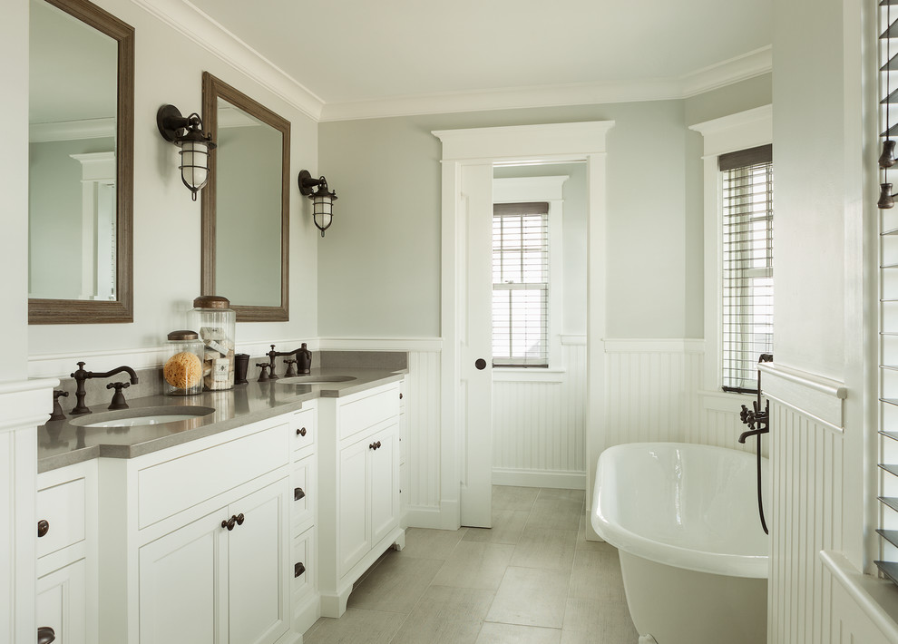 Foto på ett stort maritimt grå en-suite badrum, med ett undermonterad handfat, luckor med infälld panel, vita skåp, bänkskiva i kvarts, ett fristående badkar, grå kakel, porslinskakel och klinkergolv i keramik