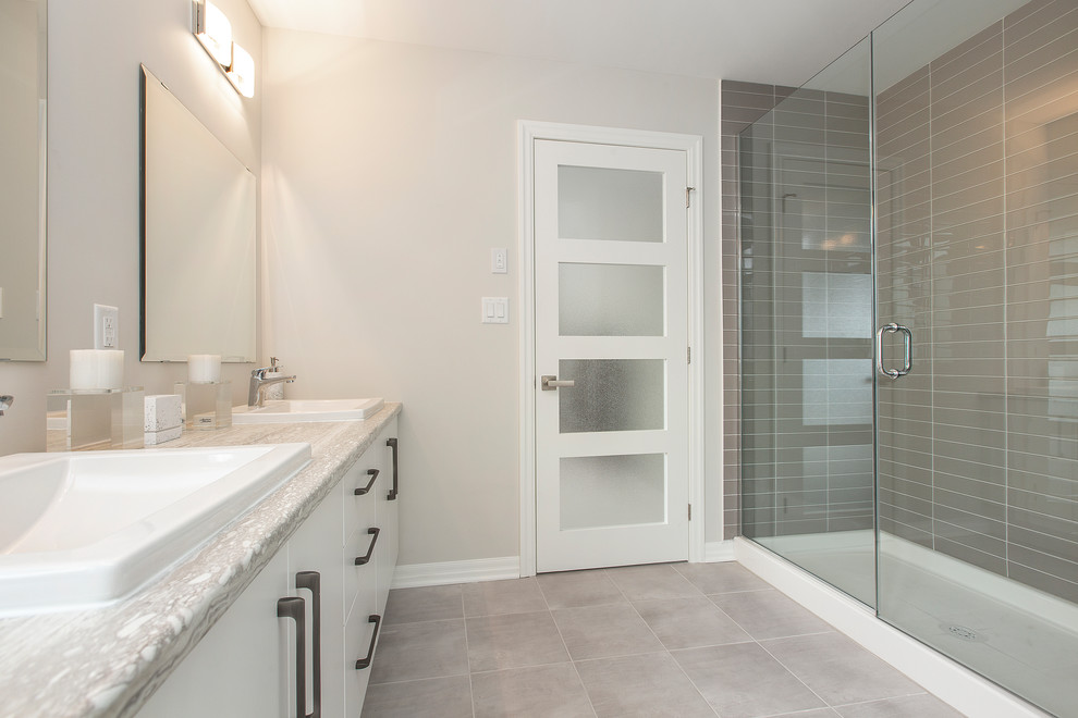 Exempel på ett stort modernt grå grått en-suite badrum, med släta luckor, vita skåp, grå väggar, klinkergolv i keramik, ett nedsänkt handfat, bänkskiva i kvarts, grått golv, en hörndusch, grå kakel, glasskiva och dusch med gångjärnsdörr