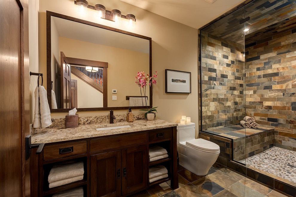 Foto på ett stort amerikanskt badrum med dusch, med ett undermonterad handfat, skåp i mörkt trä, granitbänkskiva, en toalettstol med hel cisternkåpa, brun kakel, gula väggar, skiffergolv, möbel-liknande, en dusch i en alkov och skifferkakel