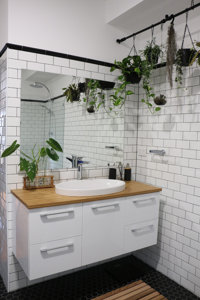 Industriell inredning av ett brun brunt en-suite badrum, med en öppen dusch, tunnelbanekakel, vita väggar, mosaikgolv, träbänkskiva, svart golv, med dusch som är öppen, släta luckor, vita skåp, vit kakel och ett nedsänkt handfat