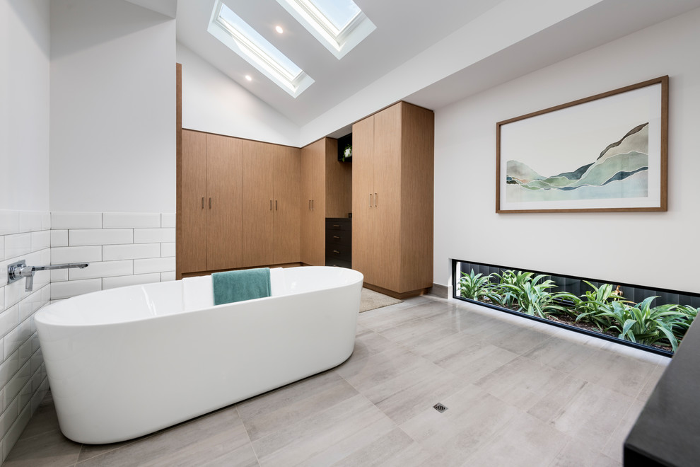 Example of a mid-sized trendy master white tile and porcelain tile ceramic tile and gray floor freestanding bathtub design in Perth with medium tone wood cabinets, white walls and black countertops