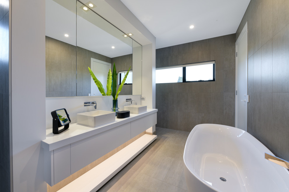 Großes Modernes Badezimmer En Suite mit flächenbündigen Schrankfronten, weißen Schränken, freistehender Badewanne, grauen Fliesen, weißer Wandfarbe, Aufsatzwaschbecken, beigem Boden, weißer Waschtischplatte, Doppelwaschbecken und schwebendem Waschtisch in Melbourne