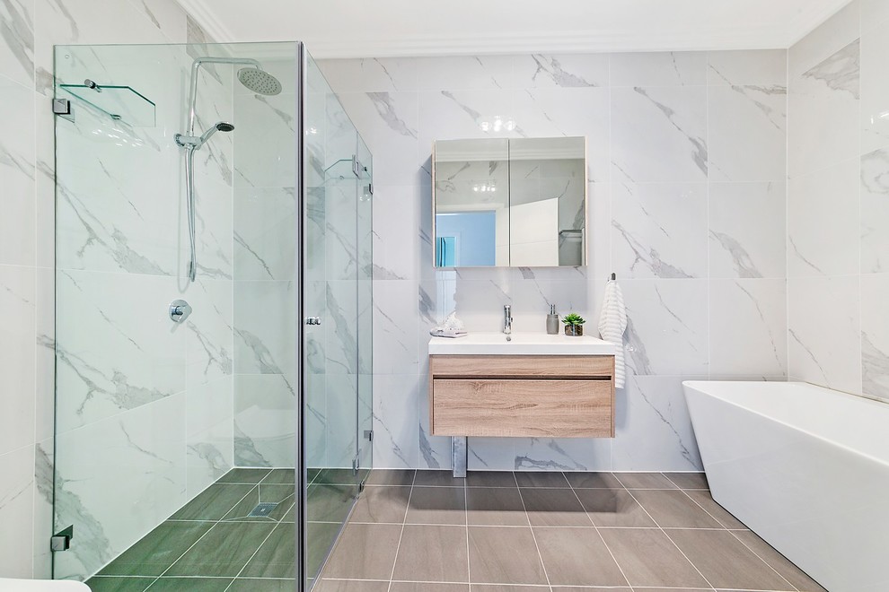 Medium sized contemporary ensuite bathroom in Sydney with flat-panel cabinets, light wood cabinets, a freestanding bath, a corner shower, a one-piece toilet, white tiles, marble tiles, white walls, ceramic flooring, an integrated sink, engineered stone worktops, grey floors, a hinged door and white worktops.