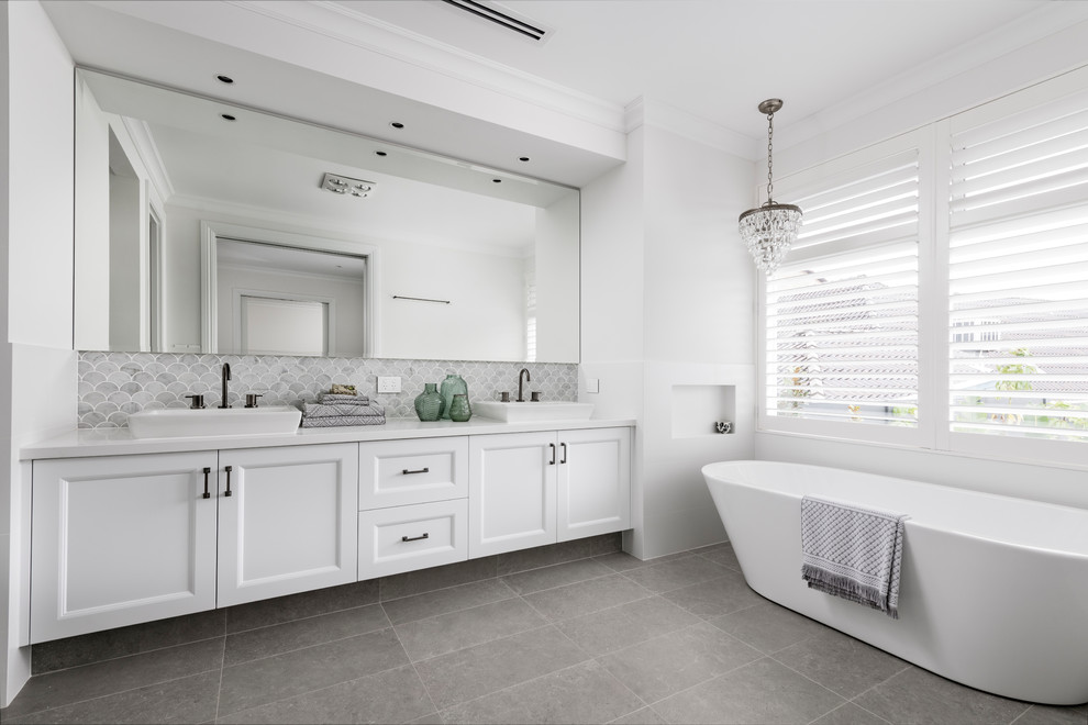 Idées déco pour une grande salle de bain classique avec un placard à porte shaker, des portes de placard blanches, une baignoire indépendante, un mur blanc, carreaux de ciment au sol, une vasque, un sol gris, un plan de toilette blanc et un carrelage gris.