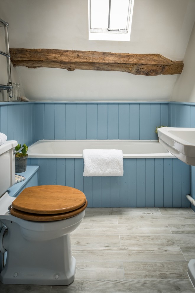Lantlig inredning av ett mellanstort badrum med dusch, med ett platsbyggt badkar, en toalettstol med separat cisternkåpa, vita väggar, ett konsol handfat och grått golv