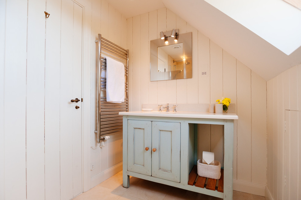 Aménagement d'une salle de bain bord de mer avec un placard avec porte à panneau encastré, des portes de placard bleues et un mur blanc.