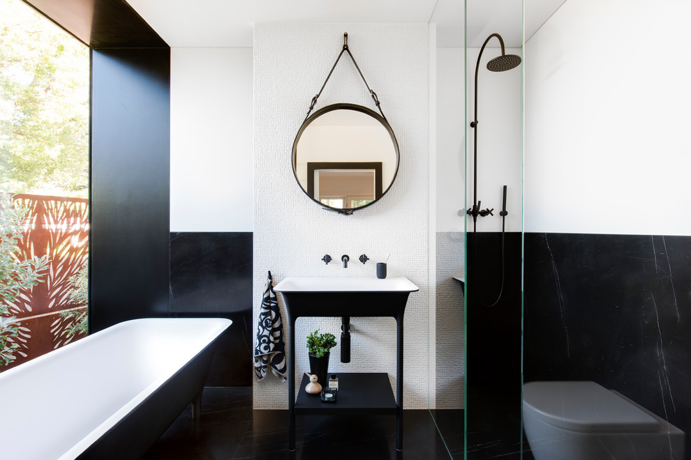 Idéer för att renovera ett litet funkis en-suite badrum, med ett fristående badkar, en öppen dusch, en vägghängd toalettstol, vit kakel, marmorkakel, vita väggar, marmorgolv, svart golv, med dusch som är öppen och ett konsol handfat