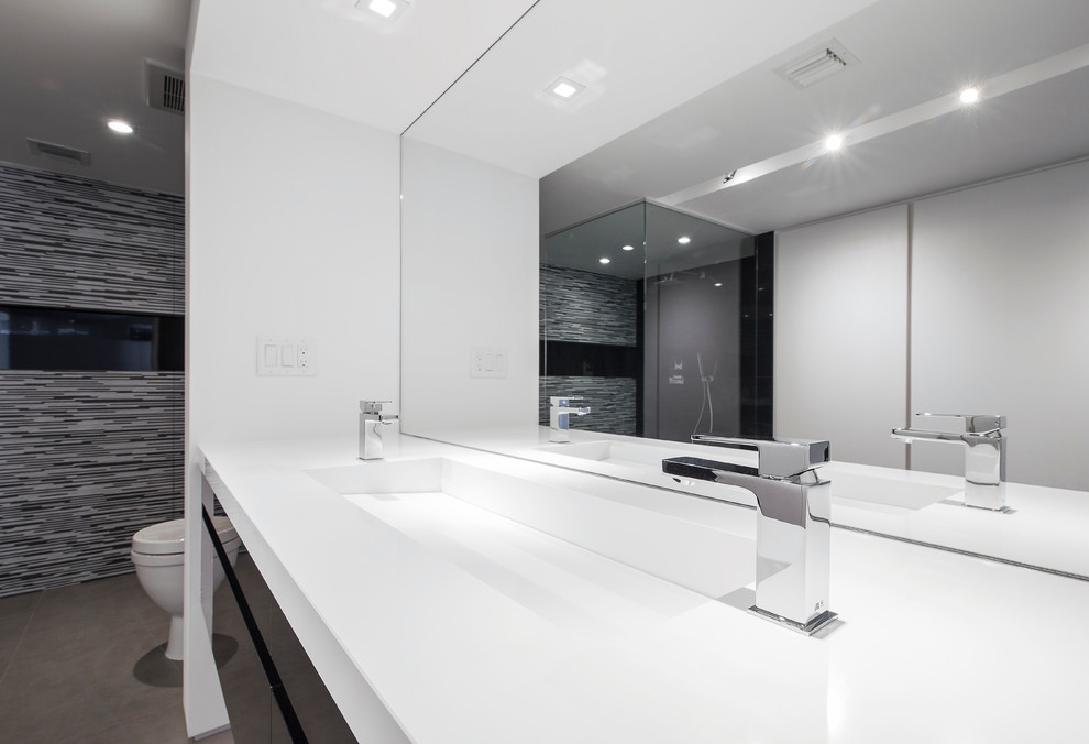 Modelo de cuarto de baño minimalista con armarios con paneles lisos, puertas de armario de madera en tonos medios, ducha empotrada, sanitario de una pieza, paredes grises, lavabo integrado y encimera de acrílico