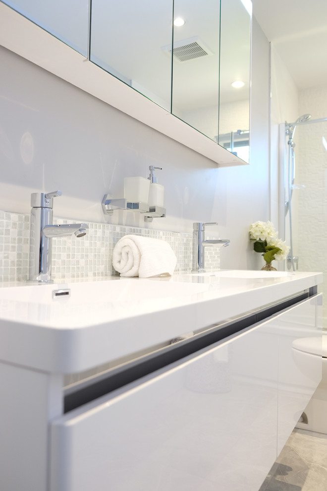 Inredning av ett modernt litet en-suite badrum, med släta luckor, vita skåp, ett badkar i en alkov, en dusch/badkar-kombination, en toalettstol med hel cisternkåpa, vit kakel, porslinskakel, grå väggar, klinkergolv i porslin, ett undermonterad handfat och bänkskiva i akrylsten