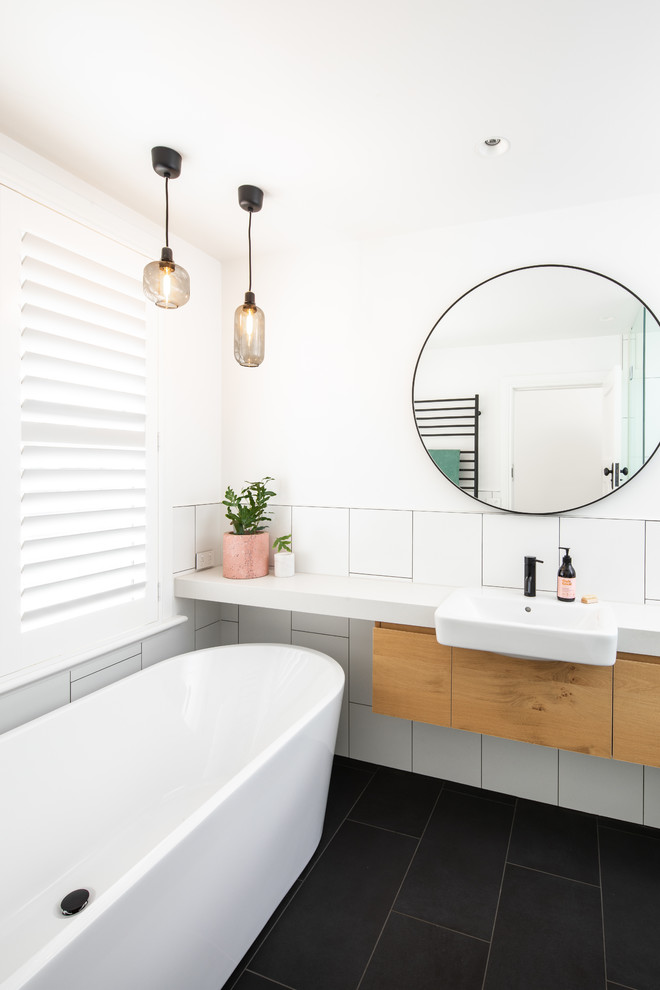 メルボルンにあるコンテンポラリースタイルのおしゃれな浴室 (フラットパネル扉のキャビネット、中間色木目調キャビネット、置き型浴槽、白いタイル、白い壁、ベッセル式洗面器、黒い床、白い洗面カウンター) の写真