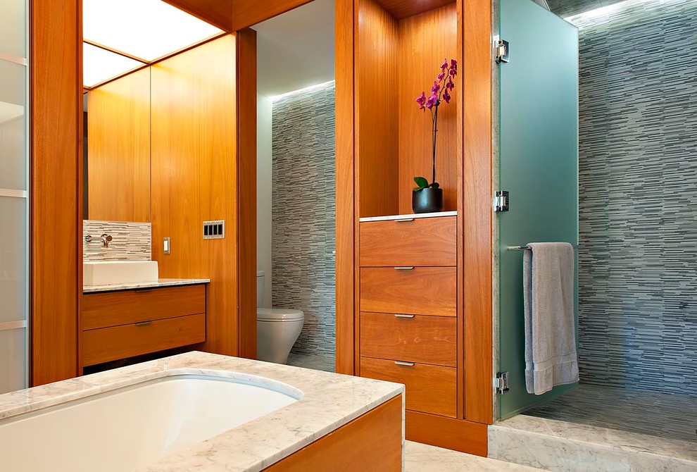На фото: большая главная ванная комната в современном стиле с настольной раковиной, плоскими фасадами, фасадами цвета дерева среднего тона, мраморной столешницей, полновстраиваемой ванной, душем в нише, унитазом-моноблоком, серой плиткой, плиткой мозаикой и мраморным полом с