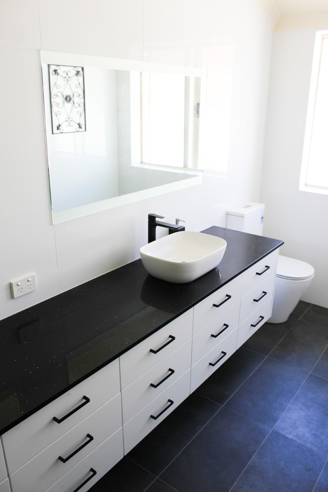 Large modern ensuite bathroom in Perth with flat-panel cabinets, white cabinets, an alcove bath, a shower/bath combination, a one-piece toilet, white tiles, ceramic tiles, white walls, porcelain flooring, a vessel sink, engineered stone worktops, black floors, a hinged door and black worktops.
