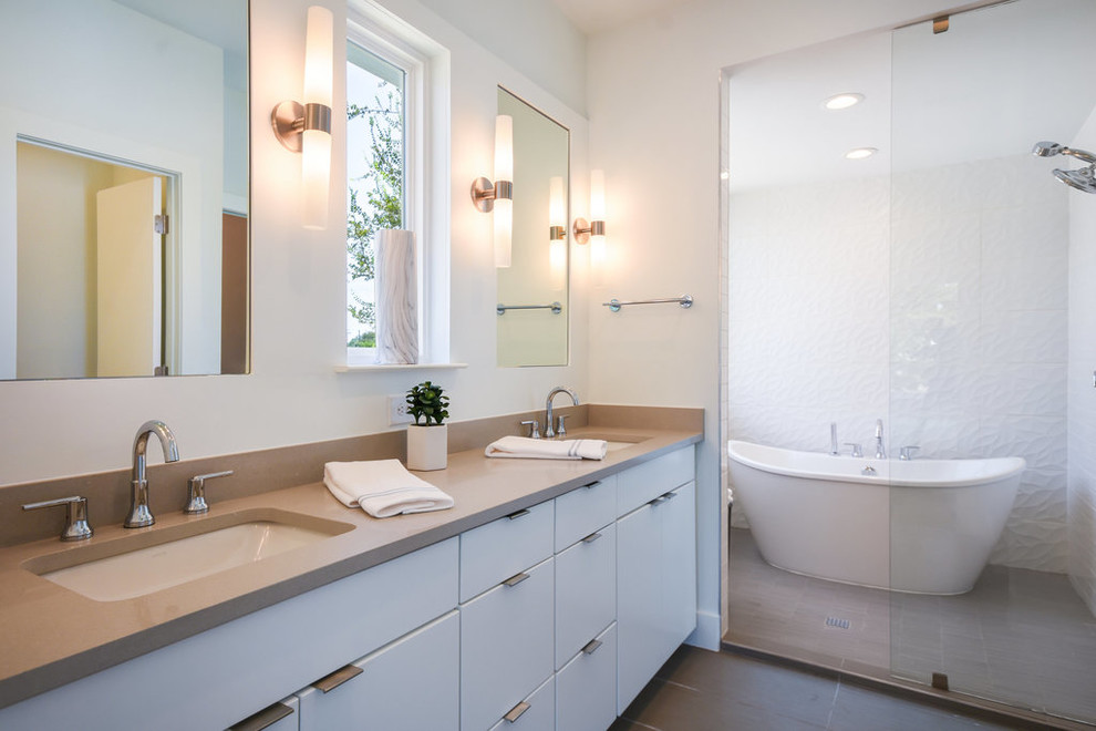 Idéer för att renovera ett mellanstort funkis beige beige en-suite badrum, med släta luckor, vita skåp, ett fristående badkar, en dusch/badkar-kombination, en toalettstol med hel cisternkåpa, vit kakel, porslinskakel, vita väggar, klinkergolv i porslin, ett undermonterad handfat, bänkskiva i kvarts, beiget golv och med dusch som är öppen
