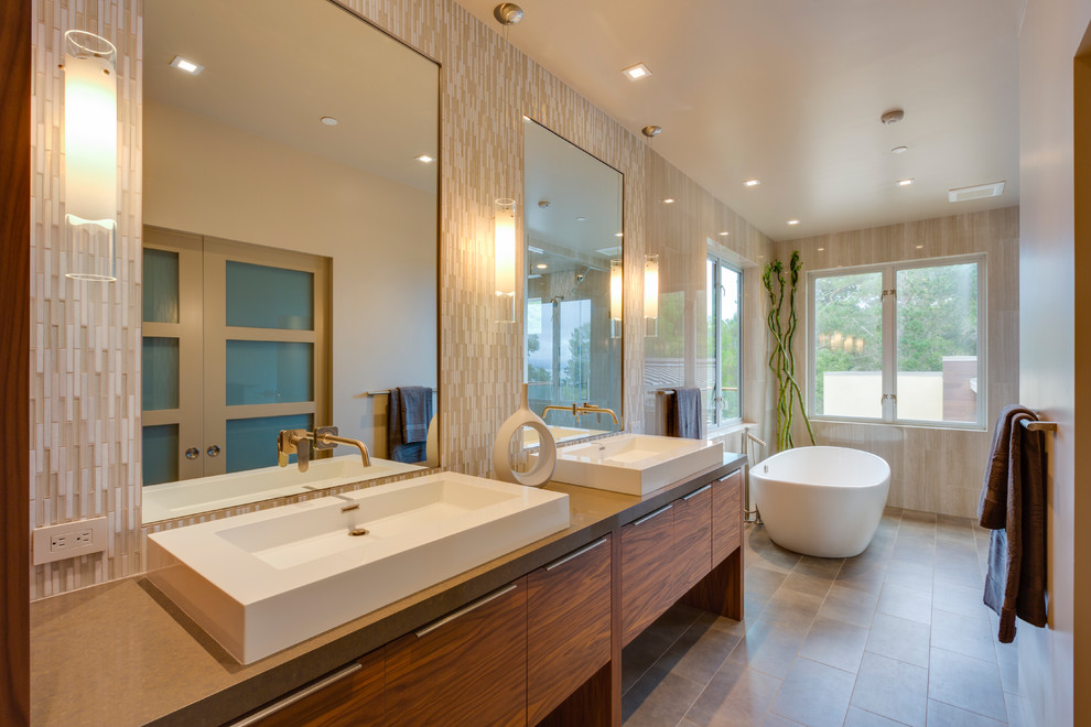 Cette image montre une salle de bain design en bois brun avec une vasque, un placard à porte plane, une baignoire indépendante, un carrelage beige, des carreaux en allumettes, un sol en carrelage de porcelaine et un plan de toilette marron.