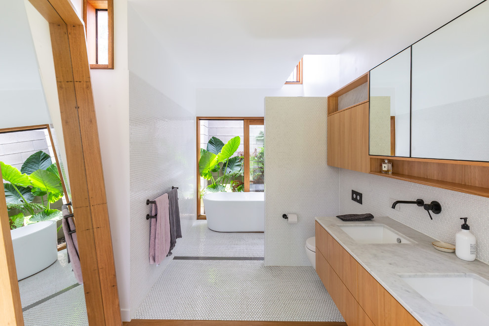 Aménagement d'une salle de bain principale moderne en bois brun avec un placard à porte plane, une baignoire indépendante, une douche ouverte, un carrelage blanc, mosaïque, un mur blanc, un sol en bois brun, un lavabo encastré, un sol marron, aucune cabine et un plan de toilette gris.