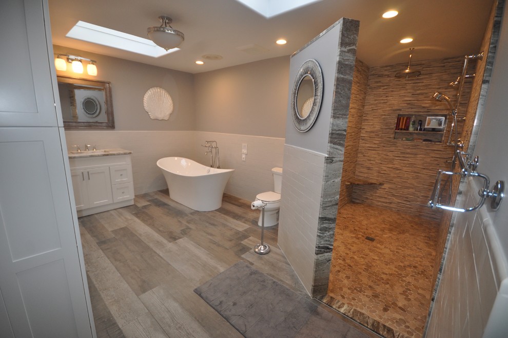 This is an example of a medium sized classic ensuite bathroom in New York with a freestanding bath, an alcove shower, a two-piece toilet, grey walls, medium hardwood flooring, a submerged sink, brown floors, an open shower and white cabinets.