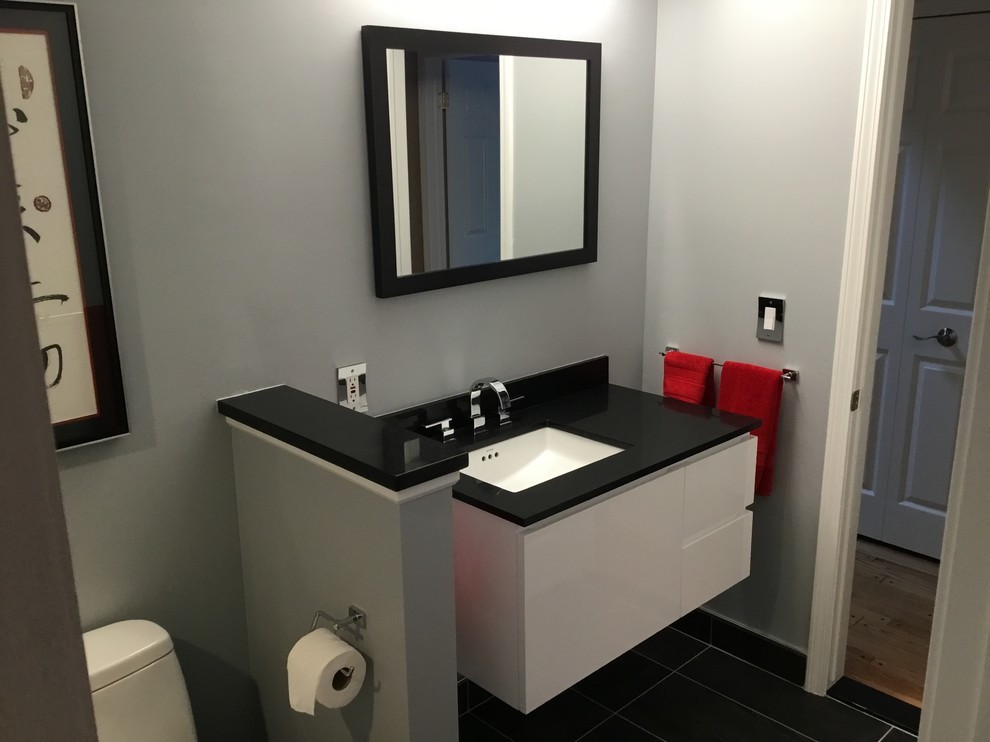 Bild på ett litet funkis en-suite badrum, med släta luckor, vita skåp, en dusch i en alkov, svart och vit kakel, kakelplattor, ett undermonterad handfat, dusch med gångjärnsdörr, ett urinoar, grå väggar, klinkergolv i porslin, svart golv och granitbänkskiva