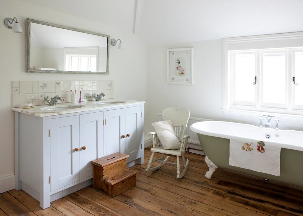 Ejemplo de cuarto de baño romántico con lavabo bajoencimera, armarios estilo shaker, puertas de armario blancas, encimera de mármol, bañera con patas, paredes blancas y suelo de madera en tonos medios