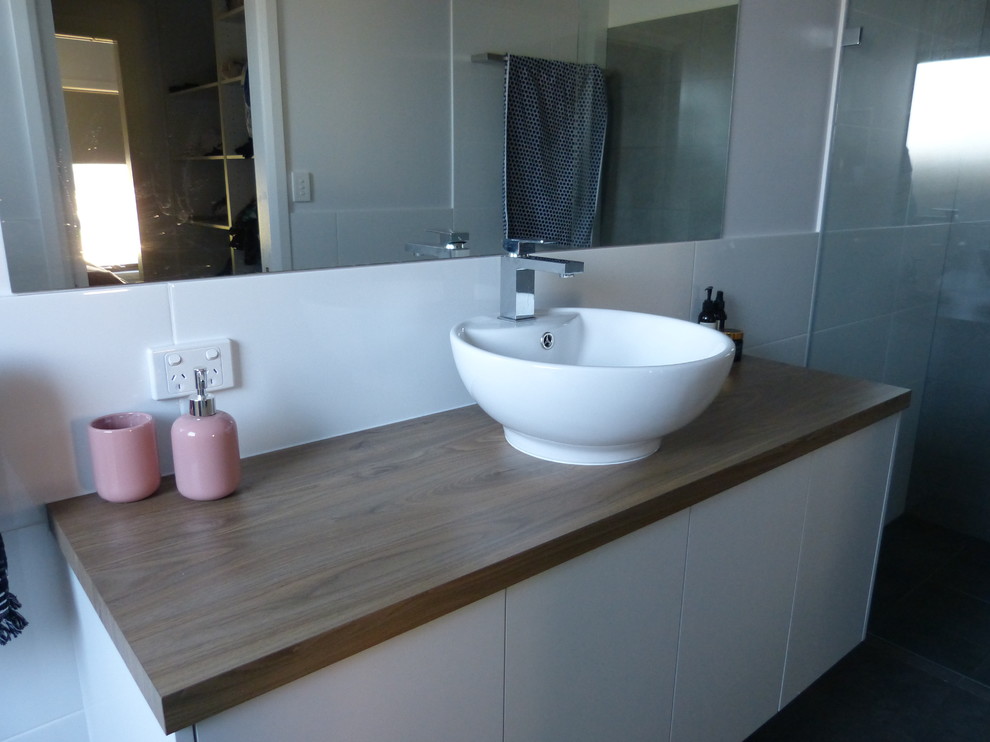 Idéer för att renovera ett mellanstort funkis brun brunt en-suite badrum, med släta luckor, vita skåp, vit kakel, porslinskakel, vita väggar, cementgolv, laminatbänkskiva och grått golv
