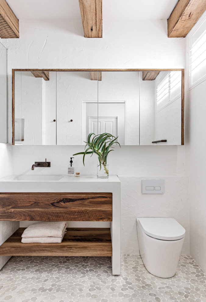 Large nautical bathroom in Sydney with open cabinets, medium wood cabinets, a walk-in shower, a one-piece toilet, white tiles, cement tiles, white walls, pebble tile flooring, an integrated sink, engineered stone worktops, beige floors, an open shower, white worktops, a wall niche, double sinks, a freestanding vanity unit and exposed beams.