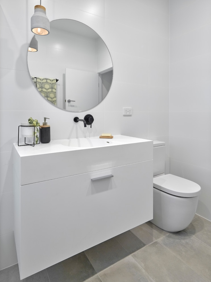 Mid-sized trendy 3/4 white tile and porcelain tile porcelain tile and gray floor bathroom photo in Other with a two-piece toilet, white walls, an integrated sink, flat-panel cabinets, white cabinets, solid surface countertops and white countertops