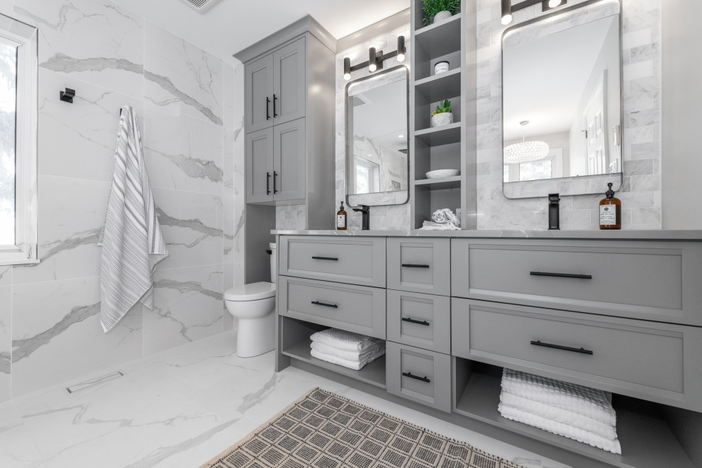 Medium sized country ensuite bathroom in Ottawa with recessed-panel cabinets, grey cabinets, a freestanding bath, a corner shower, a two-piece toilet, grey tiles, marble tiles, grey walls, marble flooring, a submerged sink, engineered stone worktops, grey floors, an open shower, grey worktops, double sinks and a built in vanity unit.