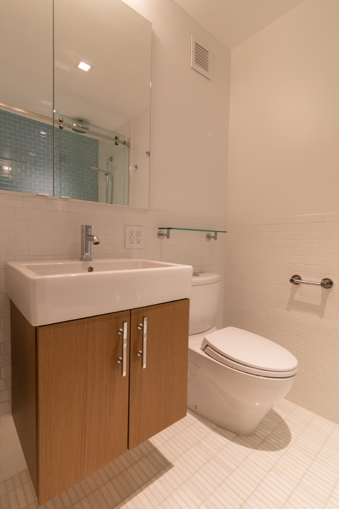 Cette image montre une salle de bain minimaliste en bois clair avec un placard à porte plane, WC séparés, un carrelage blanc, des carreaux de béton, un mur bleu, un sol en carrelage de céramique, un plan vasque, un sol blanc et une cabine de douche à porte coulissante.