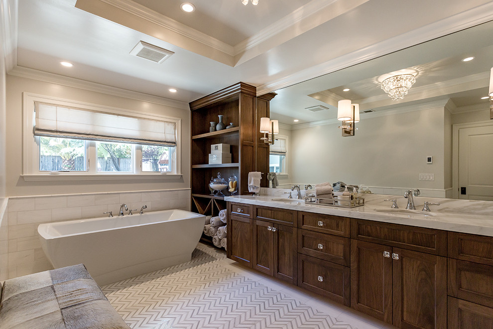 Esempio di una stanza da bagno padronale tradizionale con ante a filo, ante in legno bruno, vasca freestanding, pareti beige, lavabo sottopiano, top in marmo e pavimento bianco
