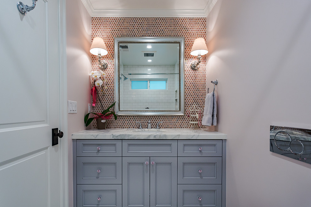 Klassisk inredning av ett badrum med dusch, med luckor med profilerade fronter, blå skåp, ett badkar i en alkov, en dusch/badkar-kombination, rosa väggar, ett undermonterad handfat och marmorbänkskiva