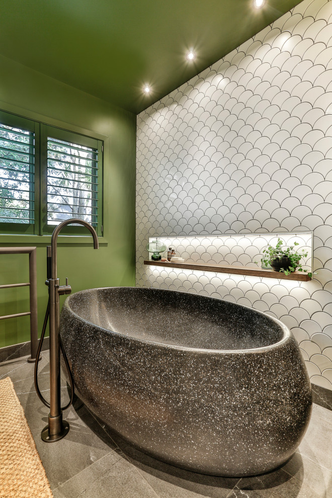 Exotisk inredning av ett mellanstort svart svart badrum med dusch, med släta luckor, svarta skåp, ett fristående badkar, en kantlös dusch, en vägghängd toalettstol, vit kakel, keramikplattor, gröna väggar, klinkergolv i porslin, ett väggmonterat handfat, bänkskiva i terrazo, svart golv och dusch med gångjärnsdörr