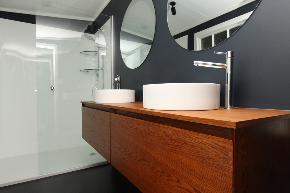 Inspiration for a medium sized modern ensuite bathroom in Auckland with freestanding cabinets, medium wood cabinets, a walk-in shower, a two-piece toilet, blue walls, vinyl flooring, a vessel sink, wooden worktops, black floors, an open shower, brown worktops, double sinks and a floating vanity unit.