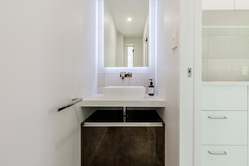 Exempel på ett litet modernt vit vitt badrum, med möbel-liknande, bruna skåp, en toalettstol med hel cisternkåpa, grå kakel, keramikplattor, vita väggar, vinylgolv, ett fristående handfat, bänkskiva i akrylsten och grått golv