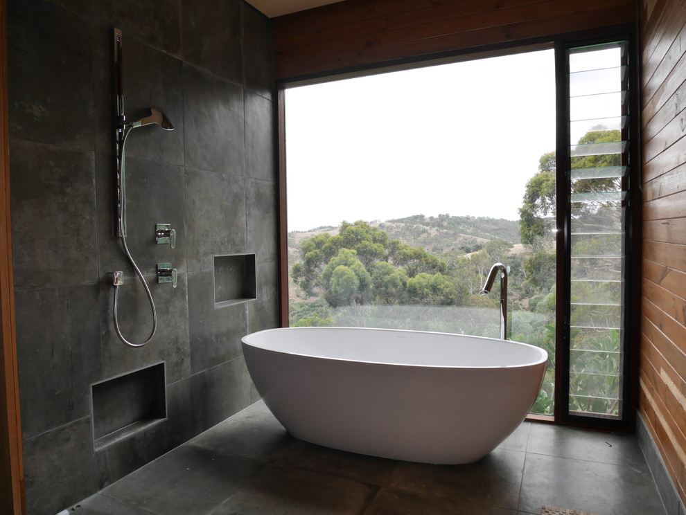 Modern inredning av ett badrum, med ett fristående badkar, grå kakel, stenkakel och grå väggar