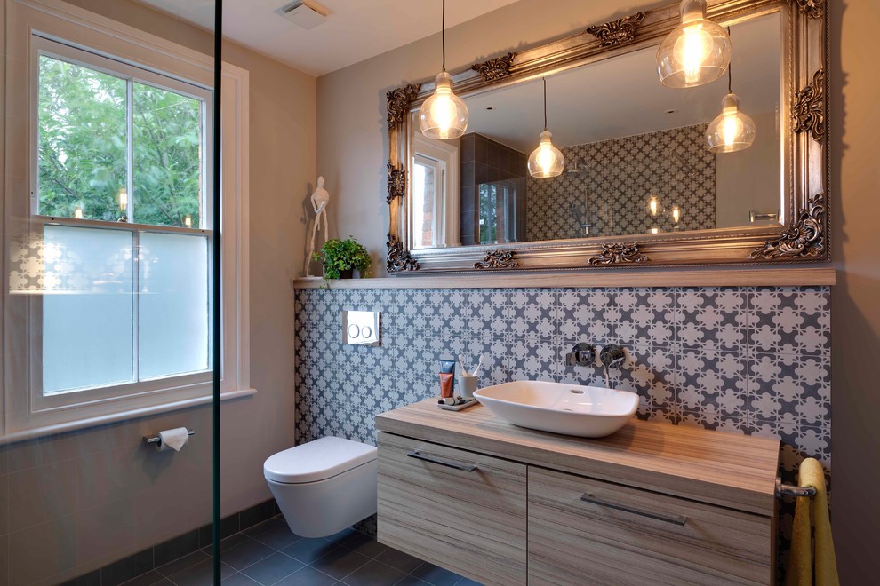 Cette image montre une salle de bain design en bois clair de taille moyenne avec un placard à porte plane, une douche ouverte, WC suspendus, un carrelage gris, des carreaux de porcelaine, un mur gris, un sol en carrelage de porcelaine, une vasque et un plan de toilette en stratifié.