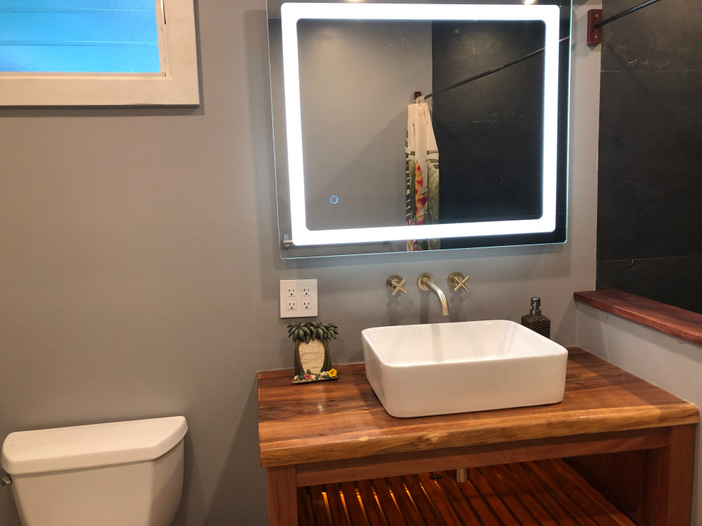 Aménagement d'une petite salle d'eau moderne en bois brun avec une douche ouverte, WC séparés, un carrelage noir, du carrelage en ardoise, une vasque, un plan de toilette en bois, meuble simple vasque et meuble-lavabo sur pied.