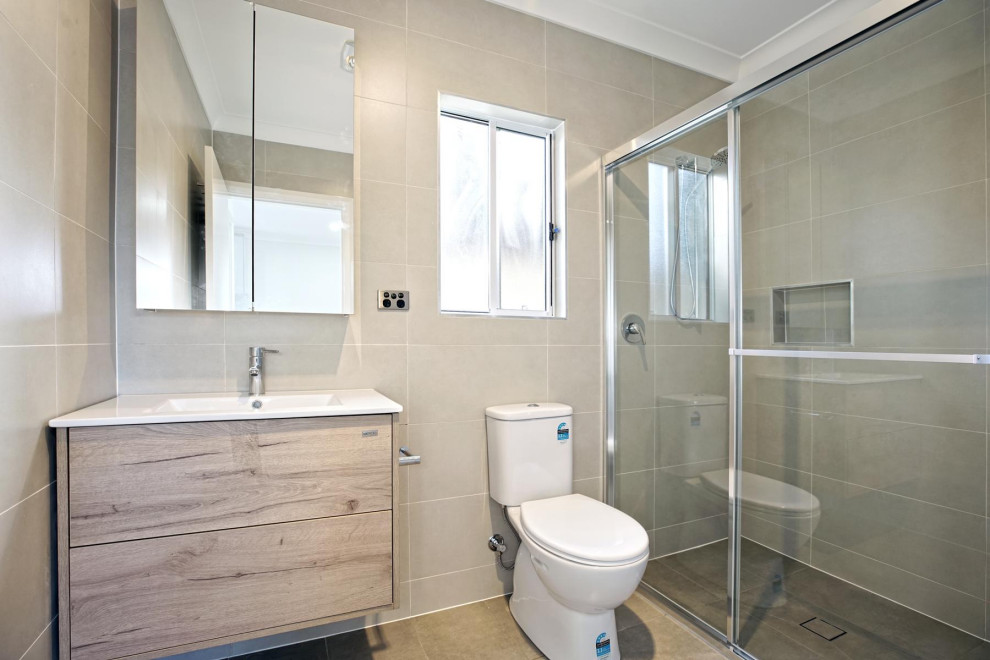 Exempel på ett litet modernt vit vitt badrum med dusch, med luckor med upphöjd panel, skåp i ljust trä, en dusch i en alkov, en toalettstol med hel cisternkåpa, grå kakel, keramikplattor, grå väggar, klinkergolv i keramik, ett integrerad handfat, bänkskiva i akrylsten, brunt golv och dusch med skjutdörr