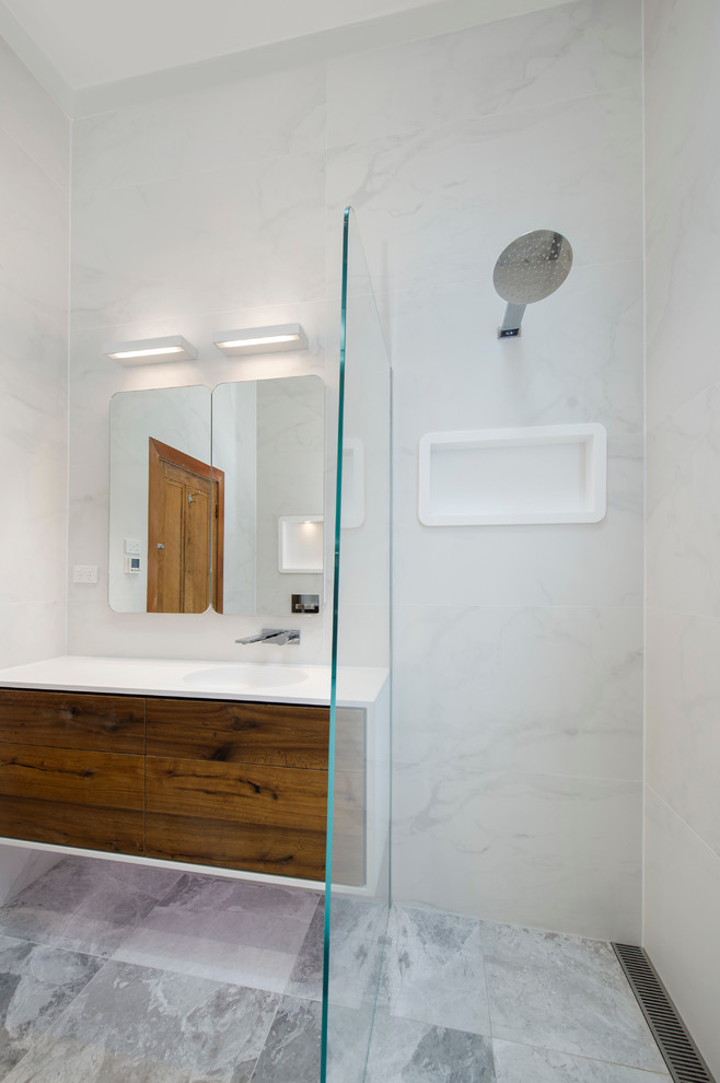 На фото: ванная комната в стиле модернизм с монолитной раковиной, фасадами цвета дерева среднего тона, столешницей из искусственного камня, открытым душем, унитазом-моноблоком, серой плиткой, керамогранитной плиткой и полом из керамогранита