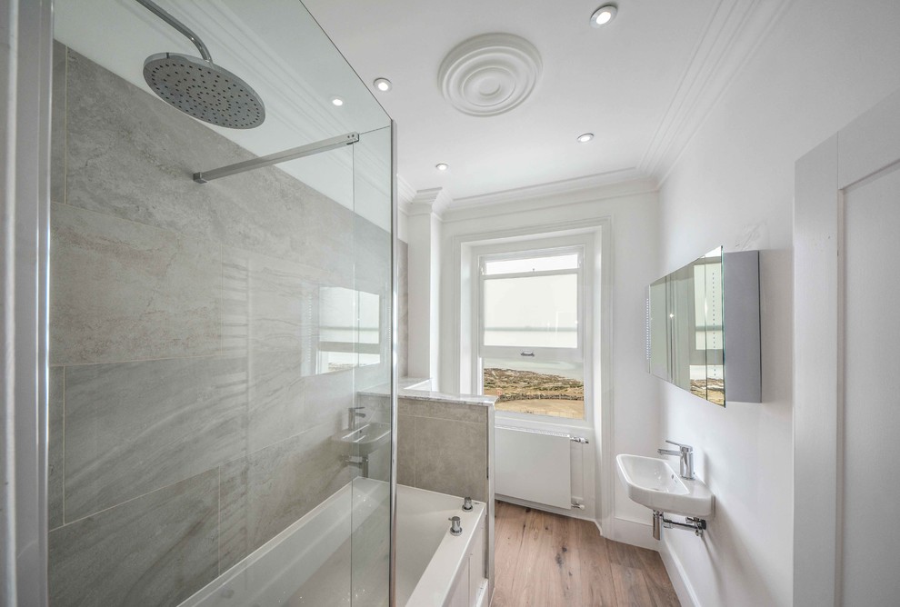 Foto de cuarto de baño principal contemporáneo grande con lavabo suspendido, bañera encastrada, combinación de ducha y bañera, sanitario de pared, baldosas y/o azulejos grises, baldosas y/o azulejos de porcelana, paredes blancas y suelo de madera clara