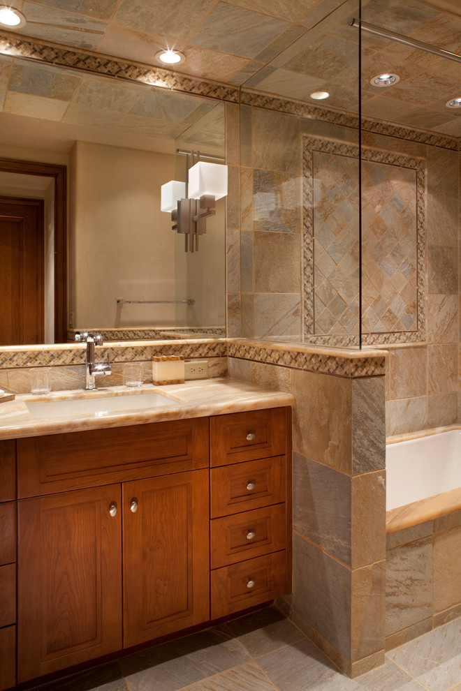 Cette image montre une salle de bain principale traditionnelle en bois brun de taille moyenne avec un placard avec porte à panneau encastré, une baignoire encastrée, un carrelage beige, des carreaux de céramique, un mur beige, un sol en carrelage de céramique, un lavabo encastré et un plan de toilette en marbre.