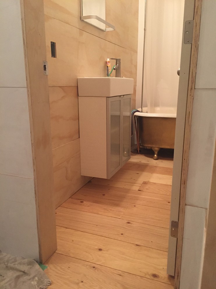 Skandinavisk inredning av ett litet badrum, med ett badkar med tassar och plywoodgolv